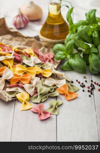 Farfalle pasta in brown paper on light wooden table background with basil and garlic and onion. Macro