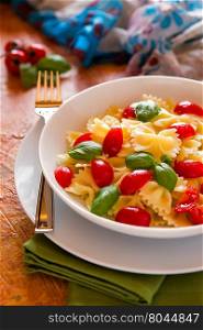 Farfalle pasta with cherry tomatoes and basil over a green napkin. Farfalle pasta with cherry tomatoes and basil