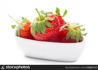 Farm fresh ripe red strawberries with attached green stalks served whole in a plain white bowl as a healthy organic snack or dessert, over white