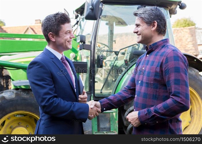 Farmer And Businessman Shaking Hands With Tractor In Background