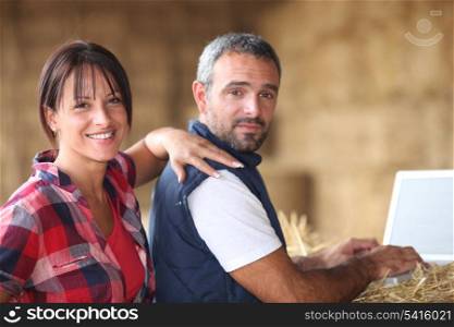Farmer couple with laptop in barn