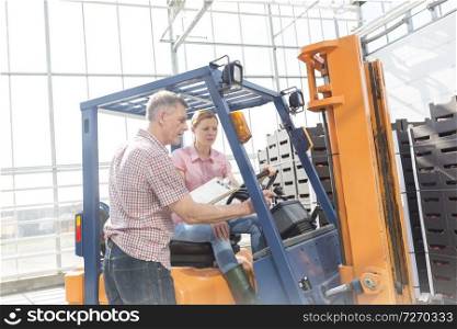 Farmer discussing with coworker on forklift over crates at storehouse