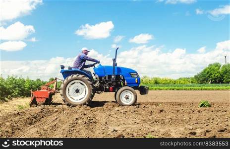 Farmer drives a tractor with a milling machine. Loosens, grind and mix soil on plantation field. Loosening surface, cultivating the land. Farming, agriculture. Field preparation for new crop planting.
