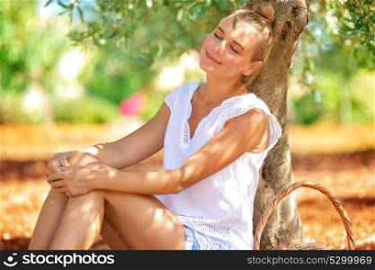 Farmer girl sleeping under an olive tree in the garden, resting in a countryside, enjoying warm sunny autumn day, harvest season