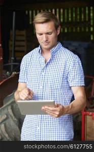 Farmer Holding Digital Tablet Standing In Barn With Old Fashioned Tractor
