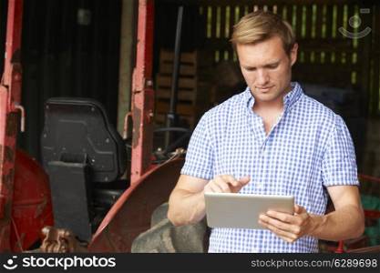 Farmer Holding Digital Tablet Standing In Barn With Old Fashioned Tractor