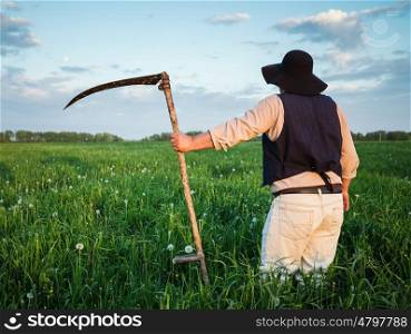 Farmer in a hat and with a scythe on green field