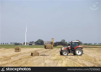 farmer in tractor busy collecting hay bales with tractor in dutch province of groningen in the netherlands