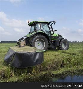 farmer mows green grassy meadow in landscape near utrecht in holland under blue sky