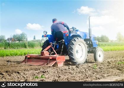 Farmer on a tractor with a milling machine processes loosens soil in the farm field. Preparation for new crop planting. Loosening surface, cultivating the land. Grind and mix soil on plantation.