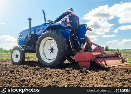 Farmer on a tractor with a milling machine processes loosens soil in the farm field. Preparation for new crop planting. Grind and mix soil on plantation. Loosening surface, cultivating the land.