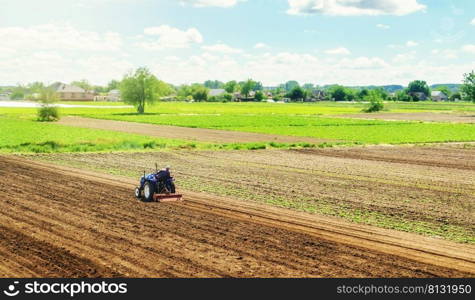 Farmer on a tractor with milling machine loosens, grinds and mixes ground. Cultivating land soil for further planting. Loosening, improving soil quality. Food production on vegetable plantations.