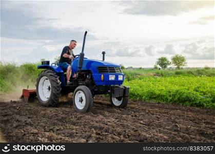 Farmer on tractor cultivates farm field. Milling soil, crushing and loosening ground before cutting rows. Farming, agriculture. Preparatory earthworks before planting a new crop. Land cultivation
