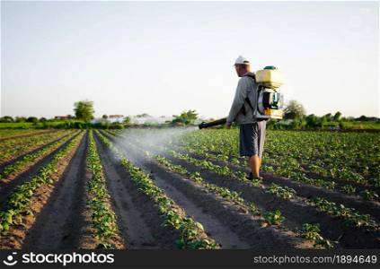 Farmer sprays pesticides on plantation. Use of chemicals for protection of plants from insects and fungal infections. Farm work on field. Agriculture and agro industry. Pesticides and fungicides.