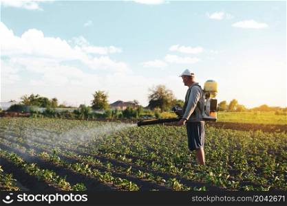 Farmer sprays pesticides on plantation. Use of chemicals for protection of plants from insects and fungal infections. Farm work on field. Pesticides and fungicides. Agriculture and agro industry.
