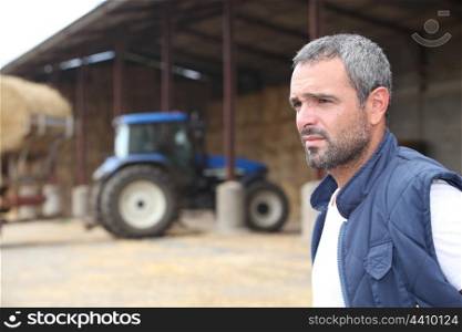 Farmer standing in front of a barn containing a tractor