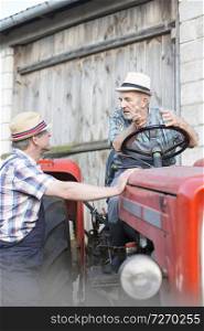 Farmer talking to coworker on tractor against barn