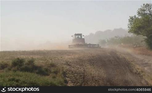 Farmer using modern farm tractor with disk harrows for harrowing field