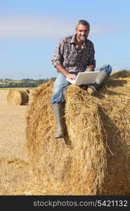 Farmer with a laptop sitting on a haystack