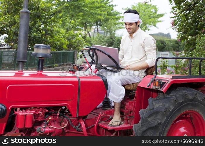 Farmer with a laptop sitting on a tractor