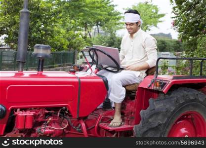 Farmer with a laptop sitting on a tractor