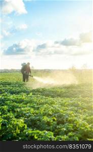 Farmer with a mist sprayer blower processes the potato plantation. Protection and care. Use of industrial chemicals to protect crops from insects and fungi. Environmental damage and chemical pollution