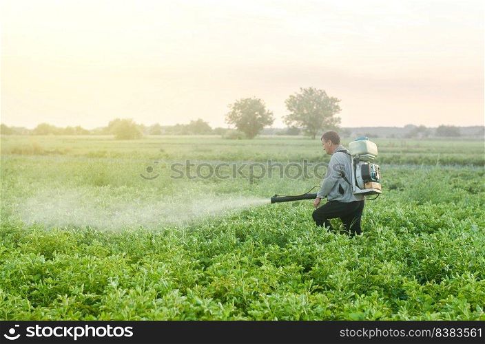 Farmer with a mist sprayer blower processes the potato plantation. Protection and care. Environmental damage and chemical pollution. Use of industrial chemicals to protect crops from insects and fungi