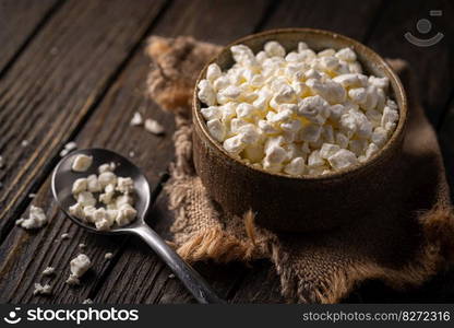 Farmers cottage cheese in a clay bowl, next to a spoon on dark wooden background, Close-up. natural healthy food, wholesome diet food. Farmers cottage cheese