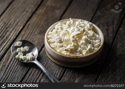 Farmers cottage cheese in a clay bowl, next to a spoon on dark wooden background, Close-up. natural healthy food, wholesome diet food. Farmers cottage cheese