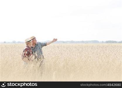 Farmers talking while standing amidst wheat crops at farm against sky