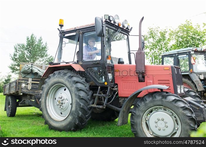 farming, agriculture and people concept - senior man driving tractor at farm