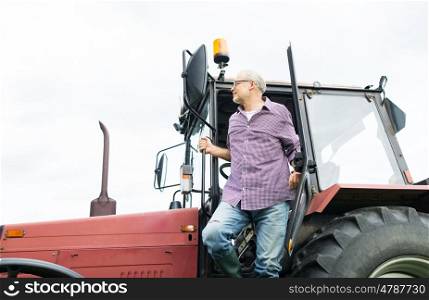 farming, agriculture and people concept - senior man or farmer getting out of tractor at farm
