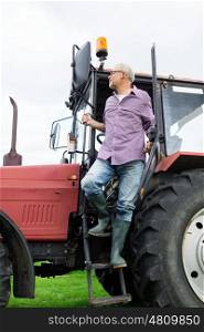 farming, agriculture and people concept - senior man or farmer getting out of tractor at farm