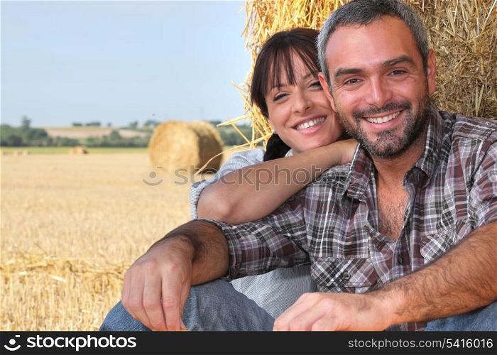 Farming couple sat by hay