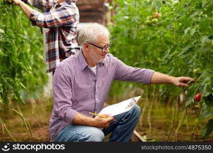 farming, gardening, agriculture and people concept - senior man with clipboard at greenhouse on farm