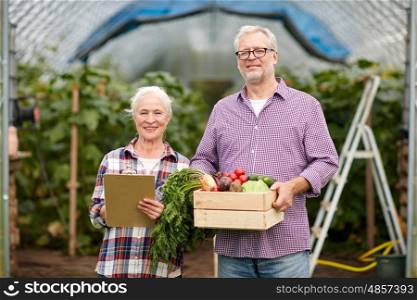 farming, gardening, agriculture, harvesting and people concept - senior couple with box of vegetables and clipboard at farm greenhouse