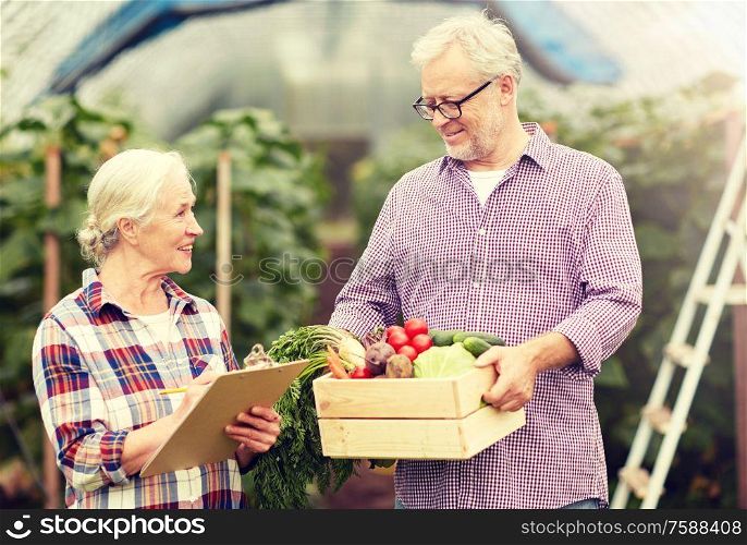 farming, gardening, agriculture, harvesting and people concept - senior couple with box of vegetables and clipboard at farm greenhouse. senior couple with box of vegetables on farm