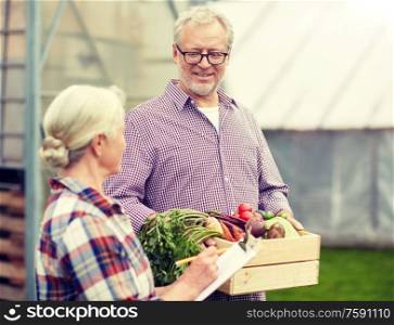 farming, gardening, agriculture, harvesting and people concept - senior couple with box of vegetables and clipboard at farm greenhouse. senior couple with box of vegetables on farm