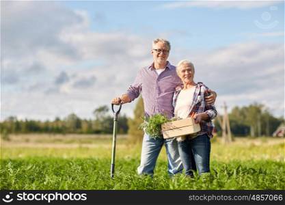 farming, gardening, agriculture, harvesting and people concept - senior couple with shovel and box of carrots at farm garden