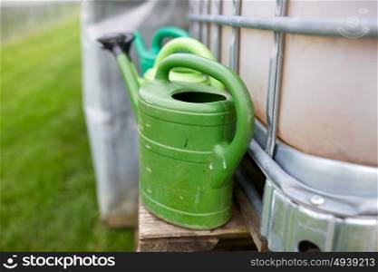 farming, gardening and agriculture concept - watering cans at farm water tank. watering cans at farm water tank