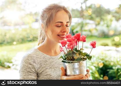 farming, gardening and people concept - happy young woman smelling pink cyclamen flowers in pot at summer garden. young woman with cyclamen flowers at summer garden