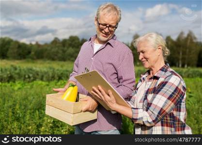 farming, gardening, harvesting, agriculture and people concept - senior couple with box of vegetables and clipboard at farm or garden