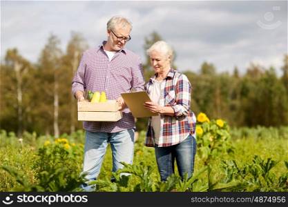 farming, gardening, harvesting, agriculture and people concept - senior couple with box of vegetables and clipboard at farm or garden