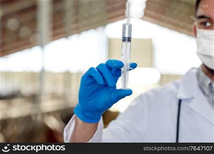 farming, medicine and animal husbandry concept - close up of veterinarian or doctor hand with vaccine in syringe on farm wearing medical mask for protection from virus. veterinarian in mask with syringe on dairy farm