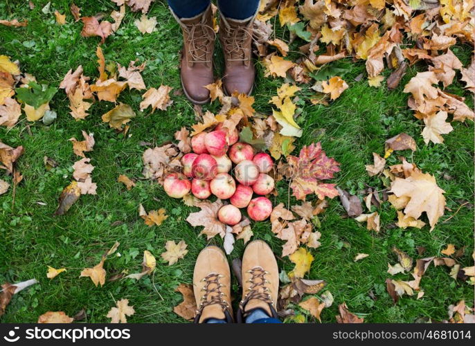 farming, season, gardening, harvesting and people concept - couple of feet in boots with apples and autumn leaves on grass