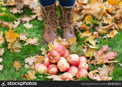 farming, season, gardening, harvesting and people concept - woman feet in boots with apples and autumn leaves