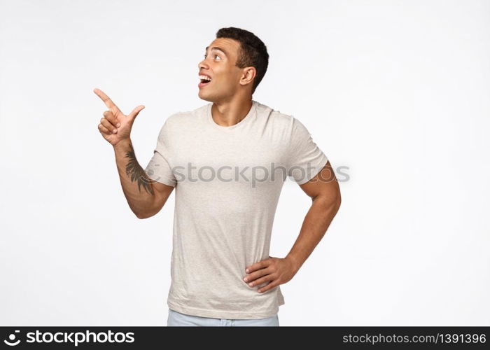 Fascinated and impressed young handsome guy in white t-shirt, pointing staring upper left corner, drop jaw and gasping from amazement as observe something interesting and unique, checking out promo.. Fascinated and impressed young handsome guy in white t-shirt, pointing staring upper left corner, drop jaw and gasping from amazement as observe something interesting and unique, checking out promo