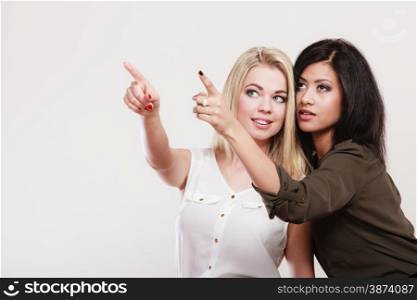 Fashion and advertisement concept. Two women caucasian and african pointing into copyspace, studio shot