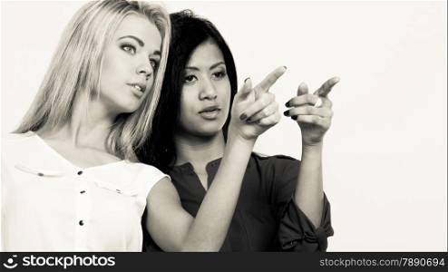 Fashion and advertisement concept. Two women caucasian and african pointing into copyspace, studio shot. Black white photo