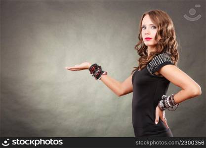 Fashion and advertising concept. Pretty young woman wearing bracelets jewellery in black elegant evening dress showing empty hand open palm with copy space